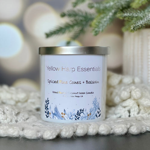 Yellow harp essentials hand poured coconut wax candle with crackling wood wick, and highly scented spiced pinecones and balsam fragrance. White glass jar with silver metal lid. ￼